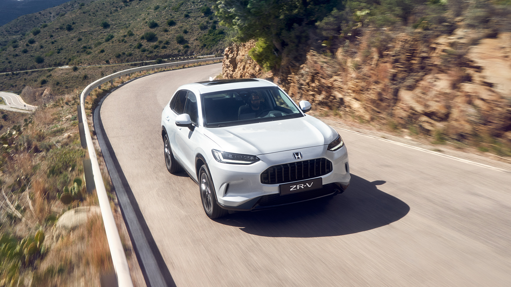 Ein weißer Honda HR-V SUV, der auf einer Auffahrt vor einem modernen Haus geparkt ist. Im Hintergrund sind Bäume und eine gepflegte Gartenanlage zu sehen. Die Szene vermittelt den Eindruck einer gehobenen Wohngegend.