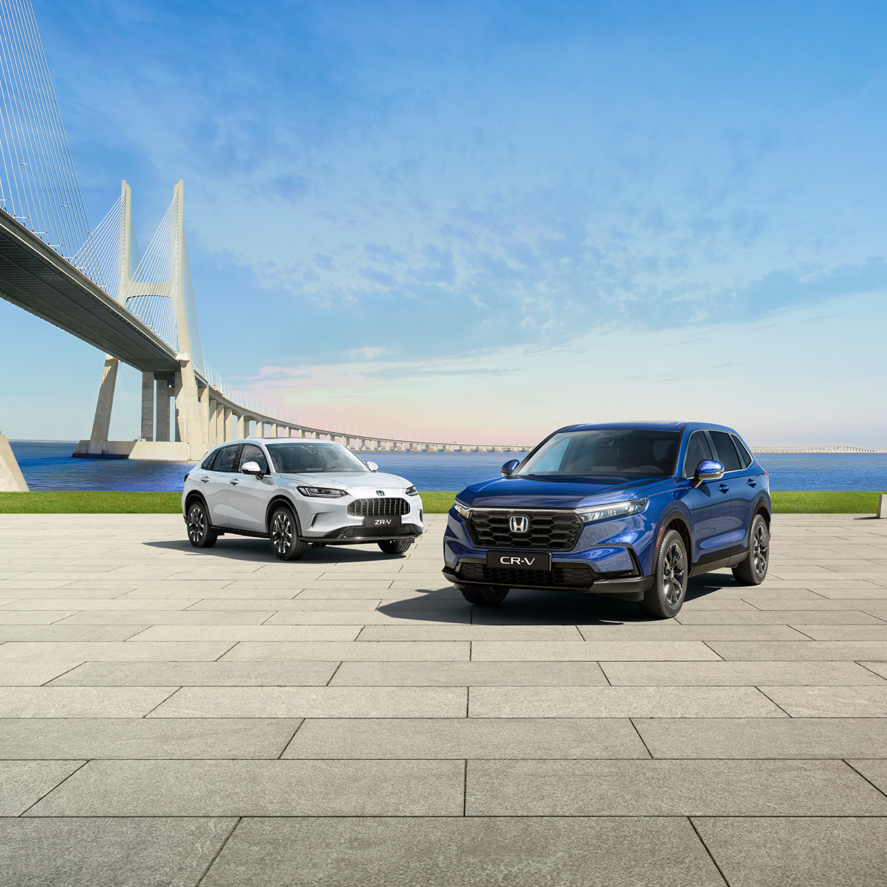 25YM ZR-V in weiß und CR-V in blau, links eine Brücke, im Hintergrund Meer