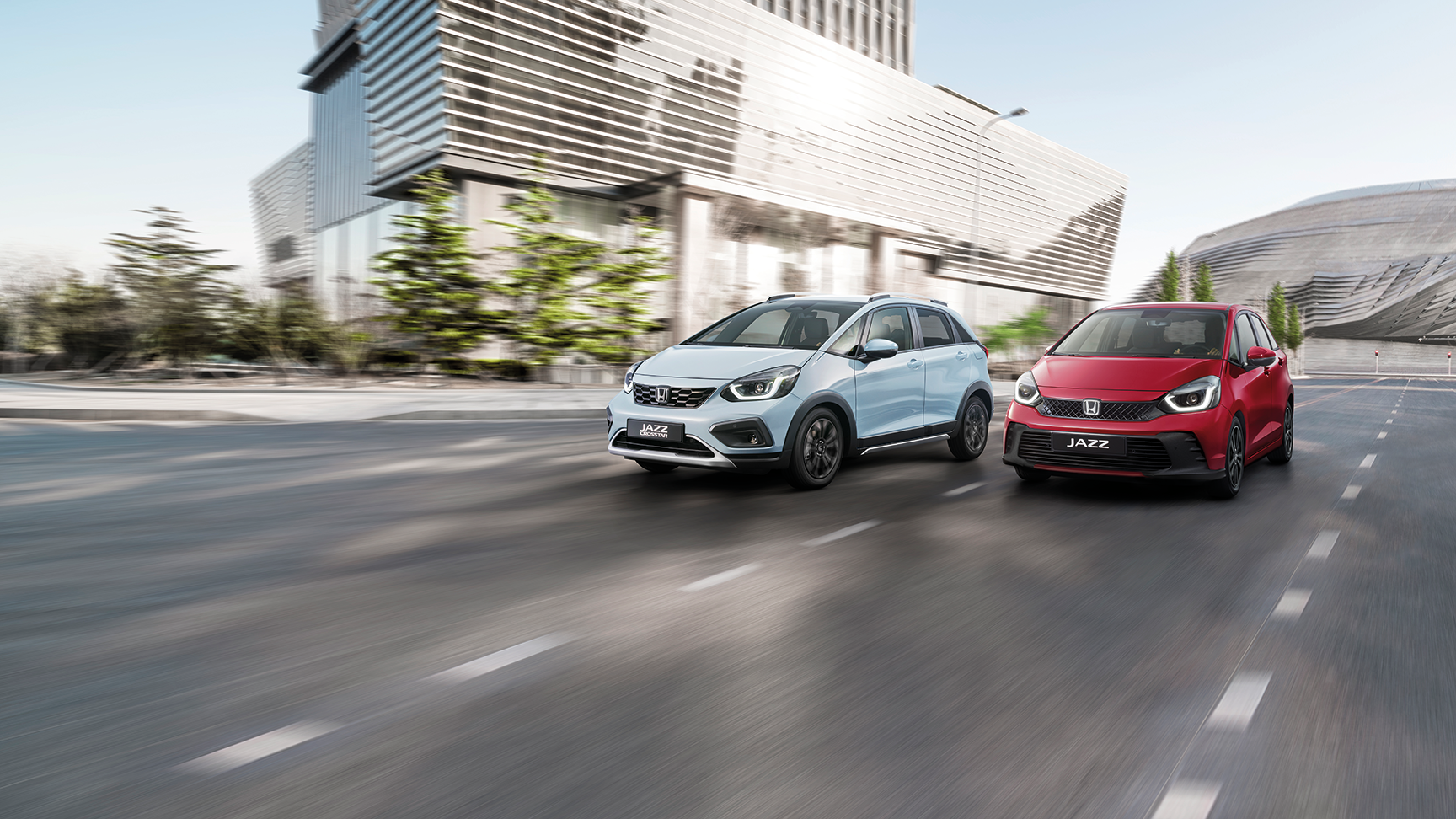 2 Honda Jazz Fahrzeuge fahren  eine Straße in der Stadt entlang.