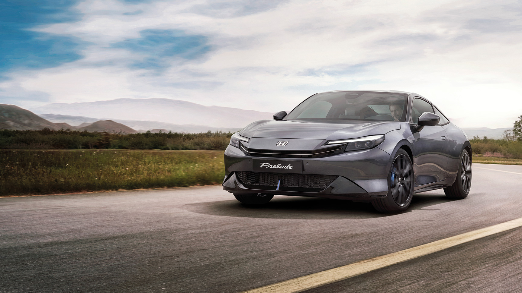 Prelude in grau fährt auf einer kurvigen Landstraße, im Hintergrund Berge