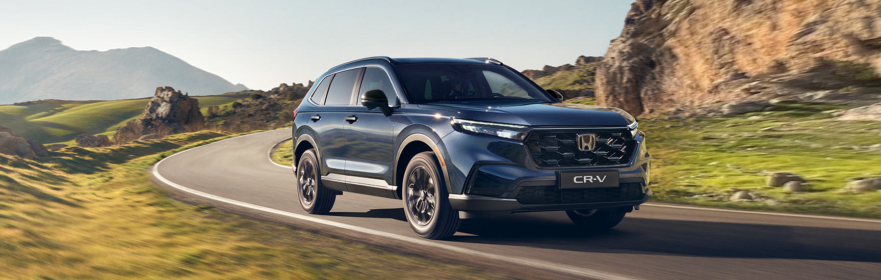 CR-V e:FHEV in blau fährt auf einer Straße am Meer entlang.