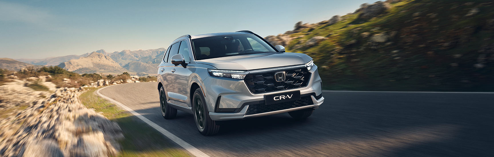 CR-V e:PHEV in weiß fährt auf einer Landstraße in einer bergigen Landschaft.