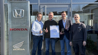Honda ehrt herausragende H&auml;ndler, Gruppe von Personen mit Urkunde vor einem Geb&auml;ude mit Aufschrift und Logo von Honda