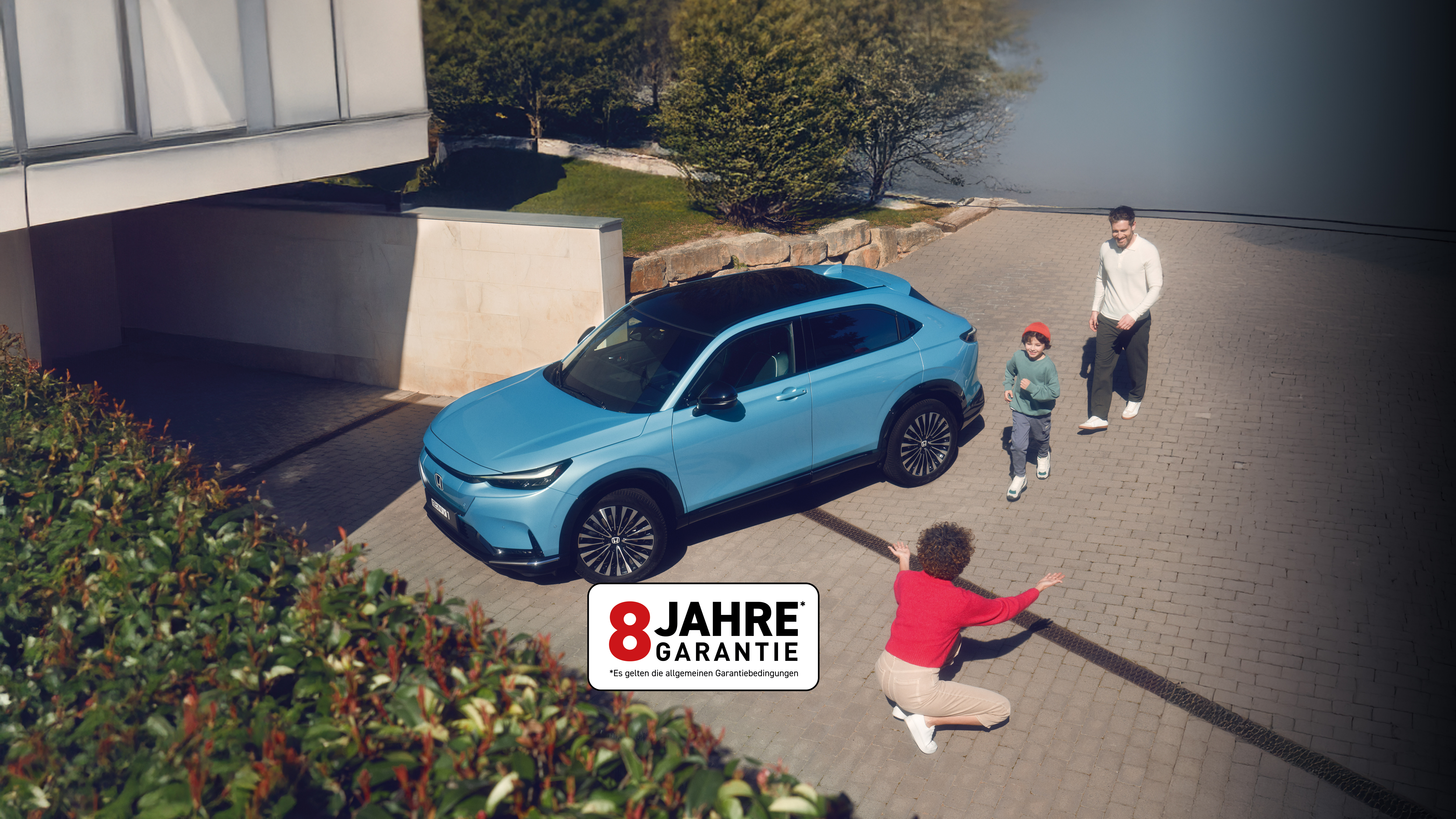 Ein hellblauer Honda e:NY1 Elektro-SUV, der in einer Einfahrt geparkt ist und um den Menschen herumlaufen. In der unteren rechten Ecke ist ein Aufkleber mit der Aufschrift „8 JAHRE GARANTIE” zu sehen.