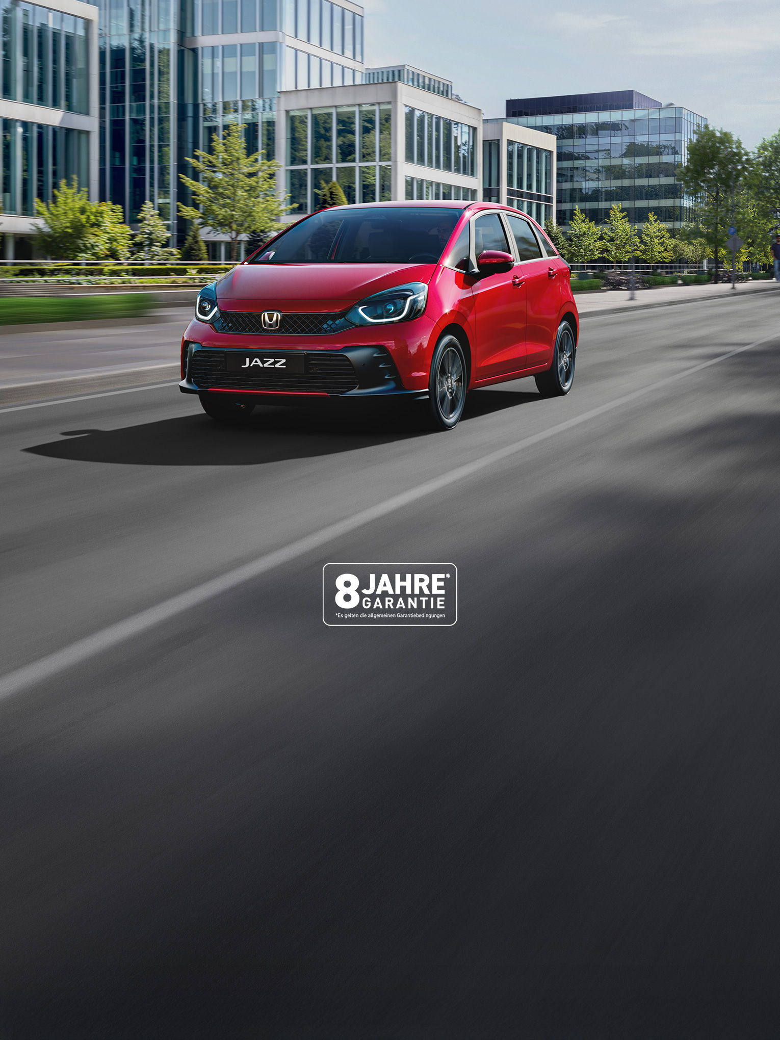 Honda Jazz in rot fährt eine Straße in einer Stadt entlang. Firmengebäude auf der linken Seite. Spaziergänger auf dem Fußweg