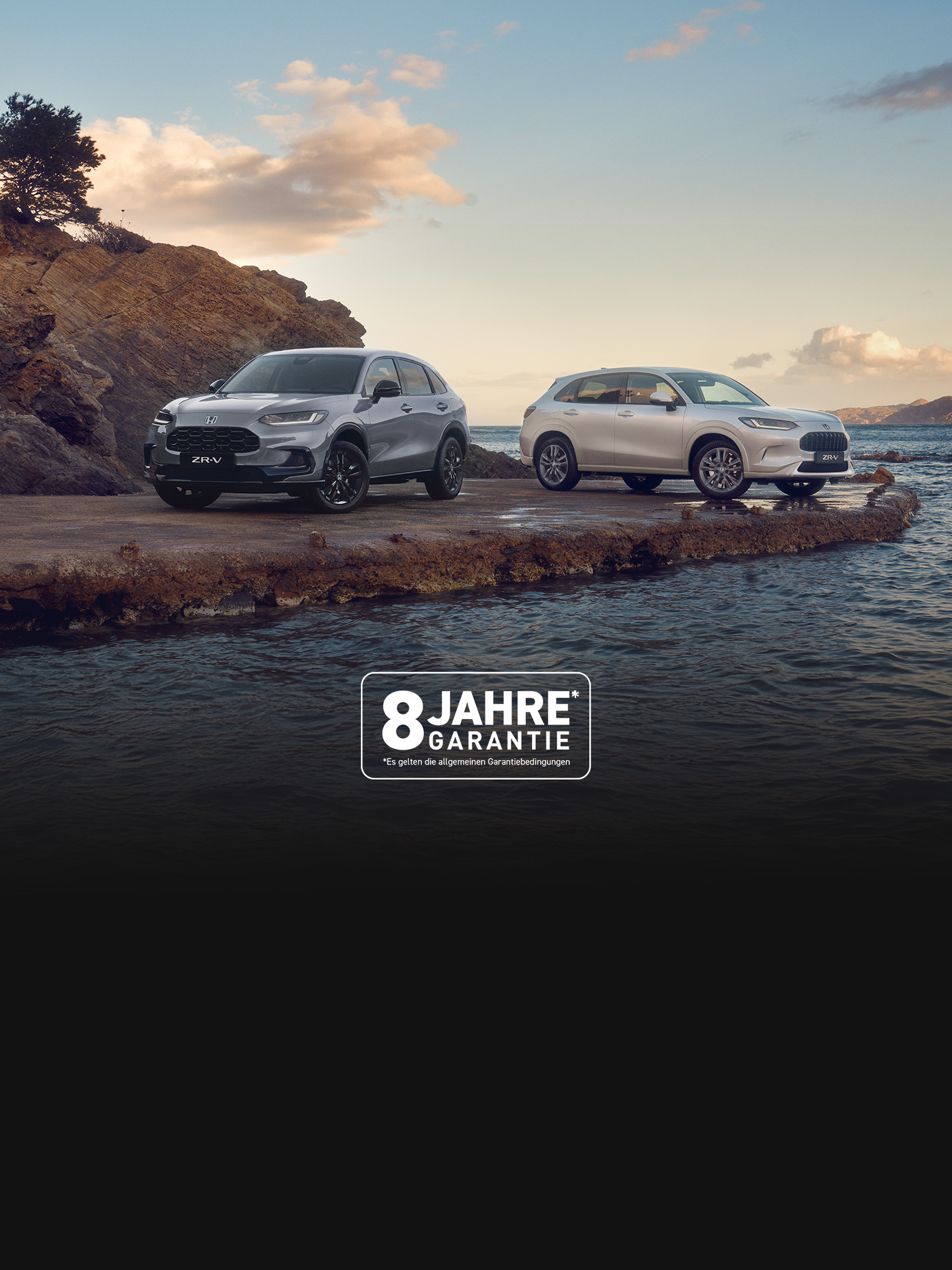 Two Honda ZR-V SUVs, one blue and one white, parked on a rocky coastal outcrop with water and hills in the background under a partly cloudy sky.