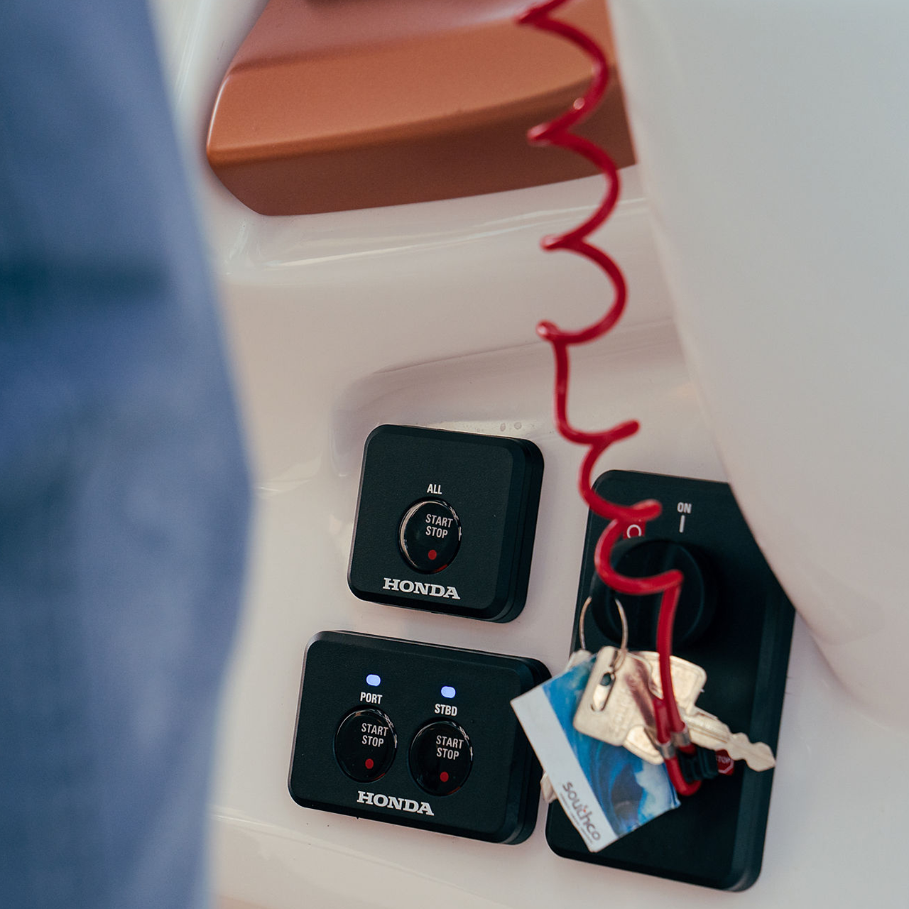 Close-up of Honda marine control panels showing start/stop buttons for engines. A key with a red spiral cord is attached to the ignition switch. The panels are labeled \"ALL\", \"PORT\", and \"STBD\" for different engine controls.