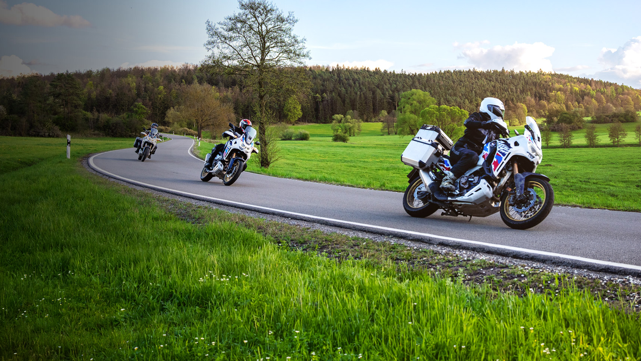 Honda Motorrräder fahren eine Staße in ländlicher Gegend entlang