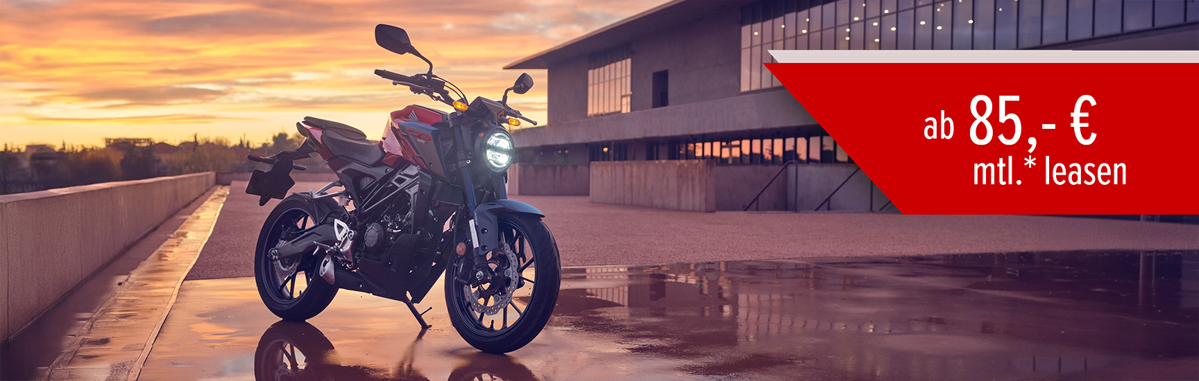 Eine Honda CB125R parkt bei Sonnenuntergang vor einem Gebäude.