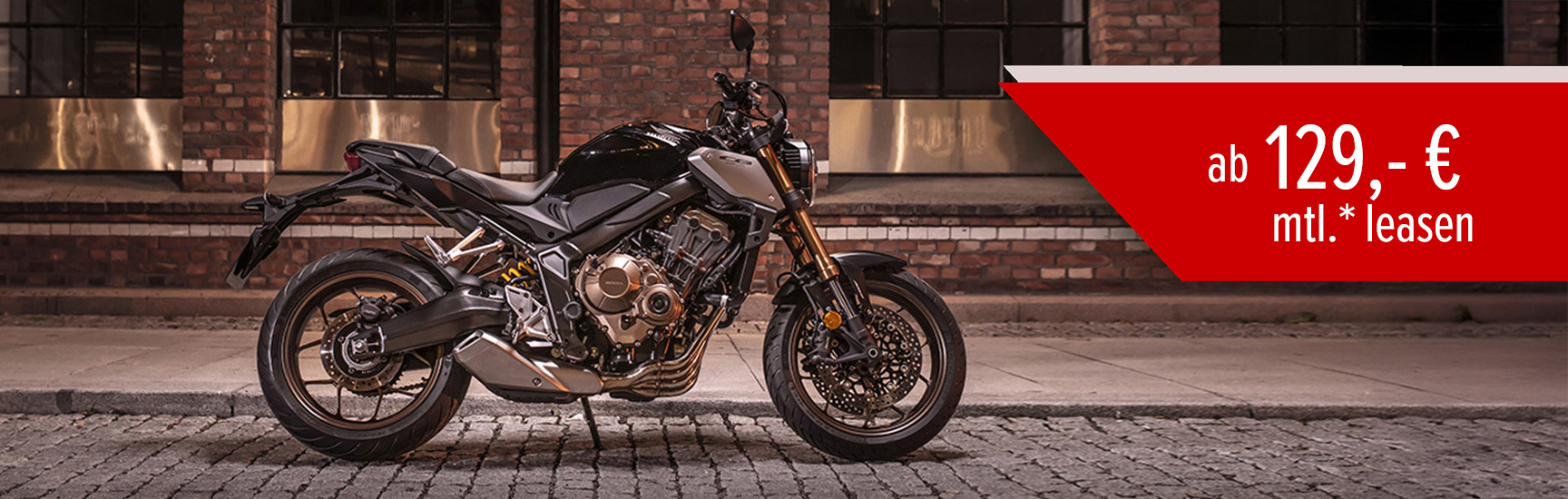 Eine Honda CB650R parkt bei Nacht vor einem Gebäude.